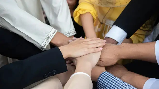 A diverse group of professionals in business attire standing together, holding hands in a display of unity and collaboration.