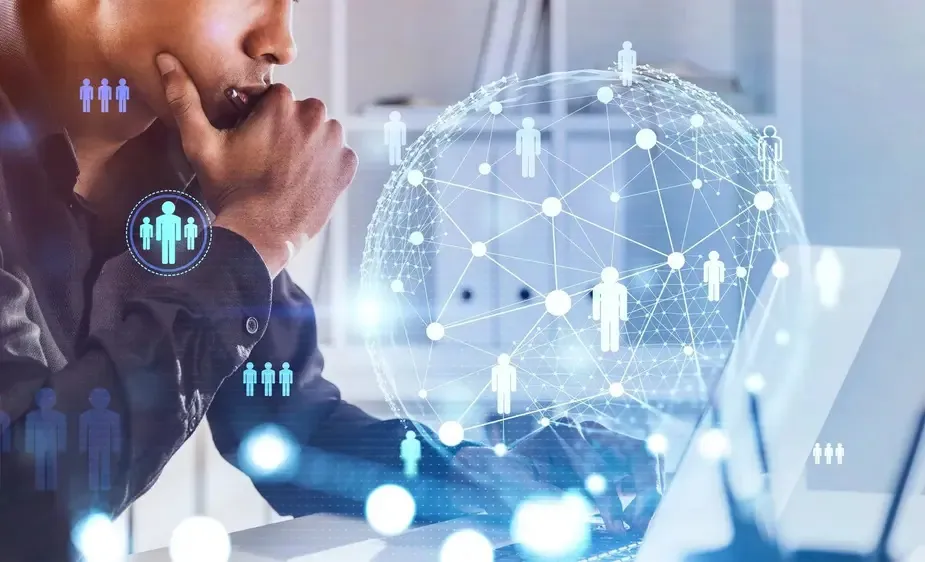 A man at a desk using a laptop, surrounded by a visual representation of a network of people.