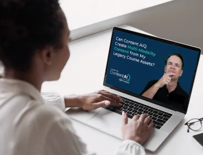 A woman works at a computer on the new AI course creator called Learning Content AIQ. A video on the computer screen features an interview of the technology.